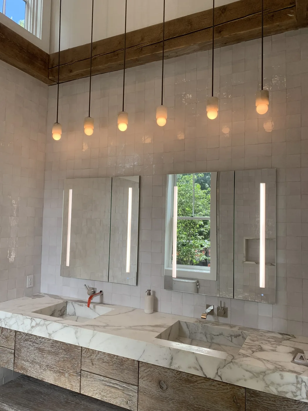 Double vanity with lit mirrors, pendant lights and a marble counter