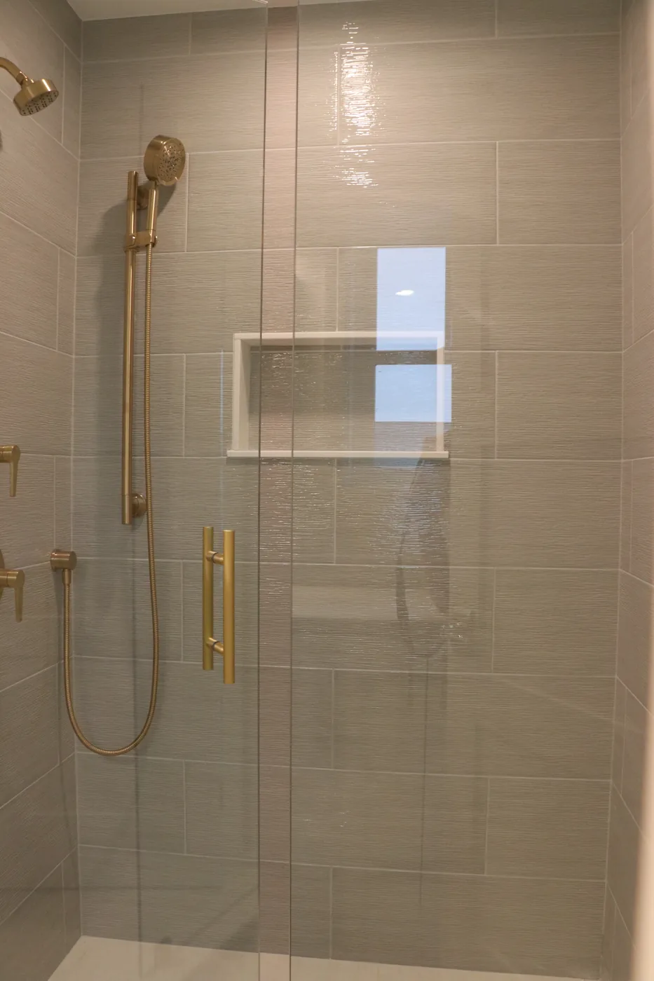 Gray tile shower with brass hand shower and niche