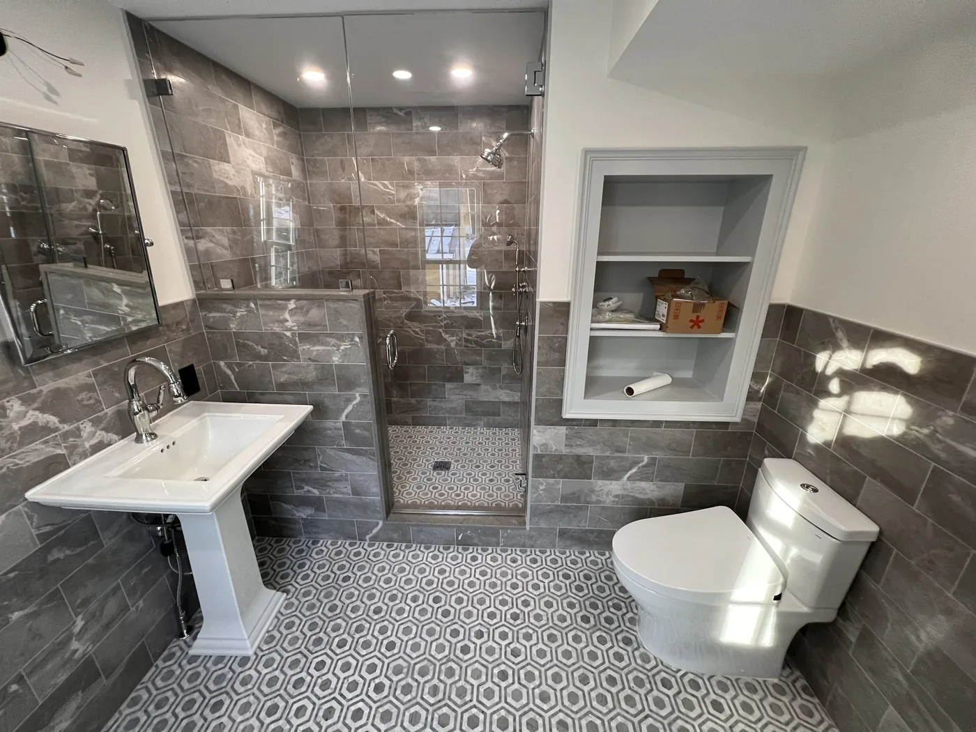 Full bathroom with gray wall tile, patterned floor and built in shelving