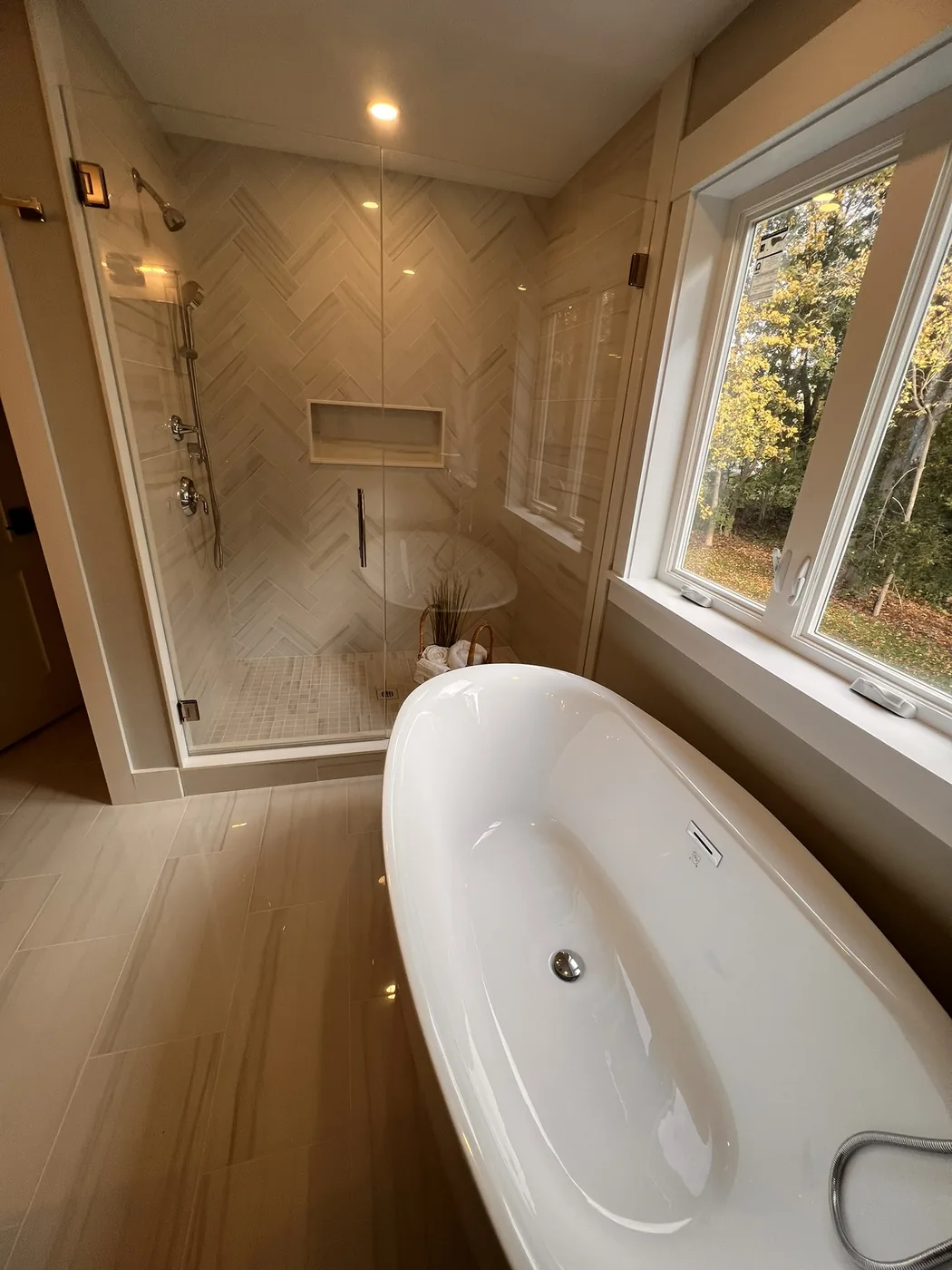 Freestanding tub beside a herringbone tile shower with a corner window
