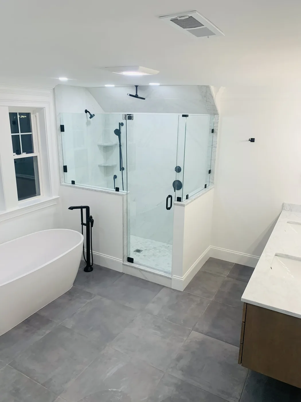 Freestanding tub and glass shower with matte black fixtures and gray tile floor