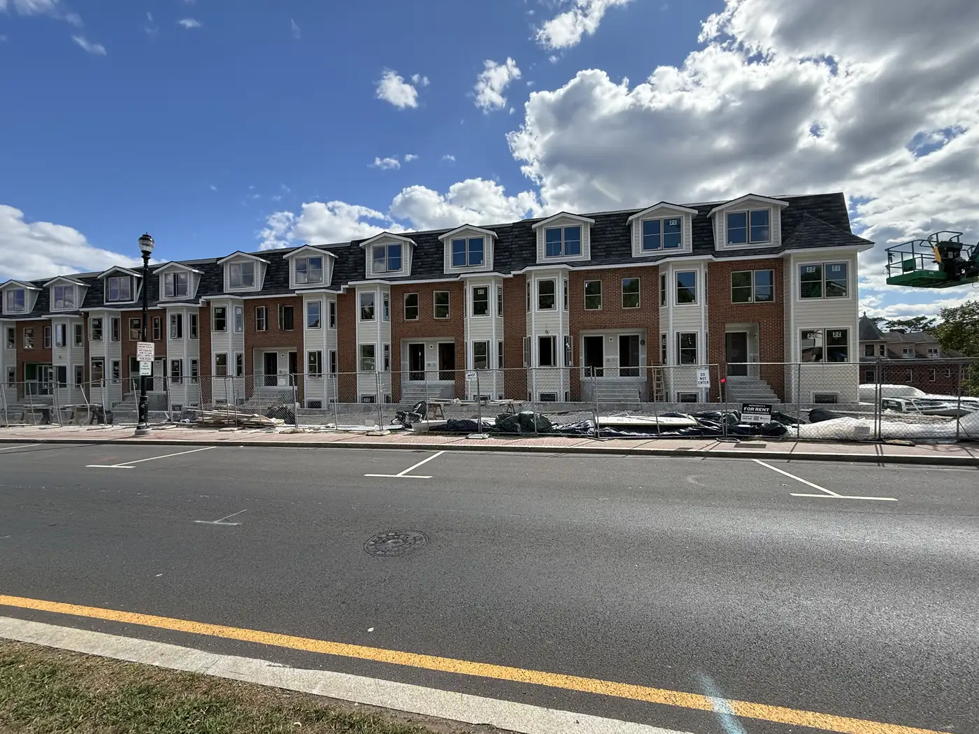 Row of new townhouses in brick and white siding, still fenced off during construction