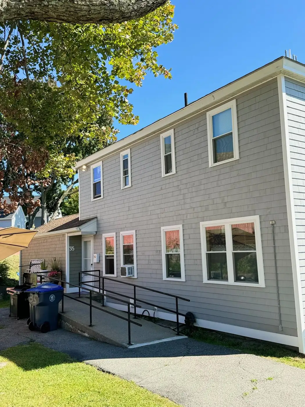Two story building in taupe shingle siding with white trim and an entry ramp