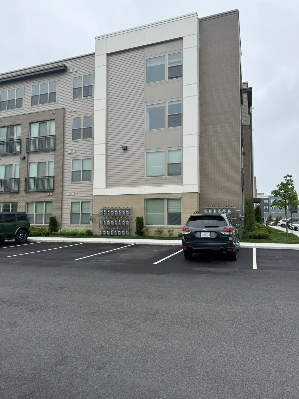 Apartment building with lap siding and panel over a brick base, seen from the parking lot